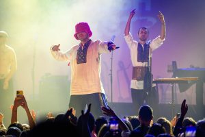 Frontman Oleh Psiuk of Kalush Orchestra rapping into a microphone while wearing a pink bucket hat.